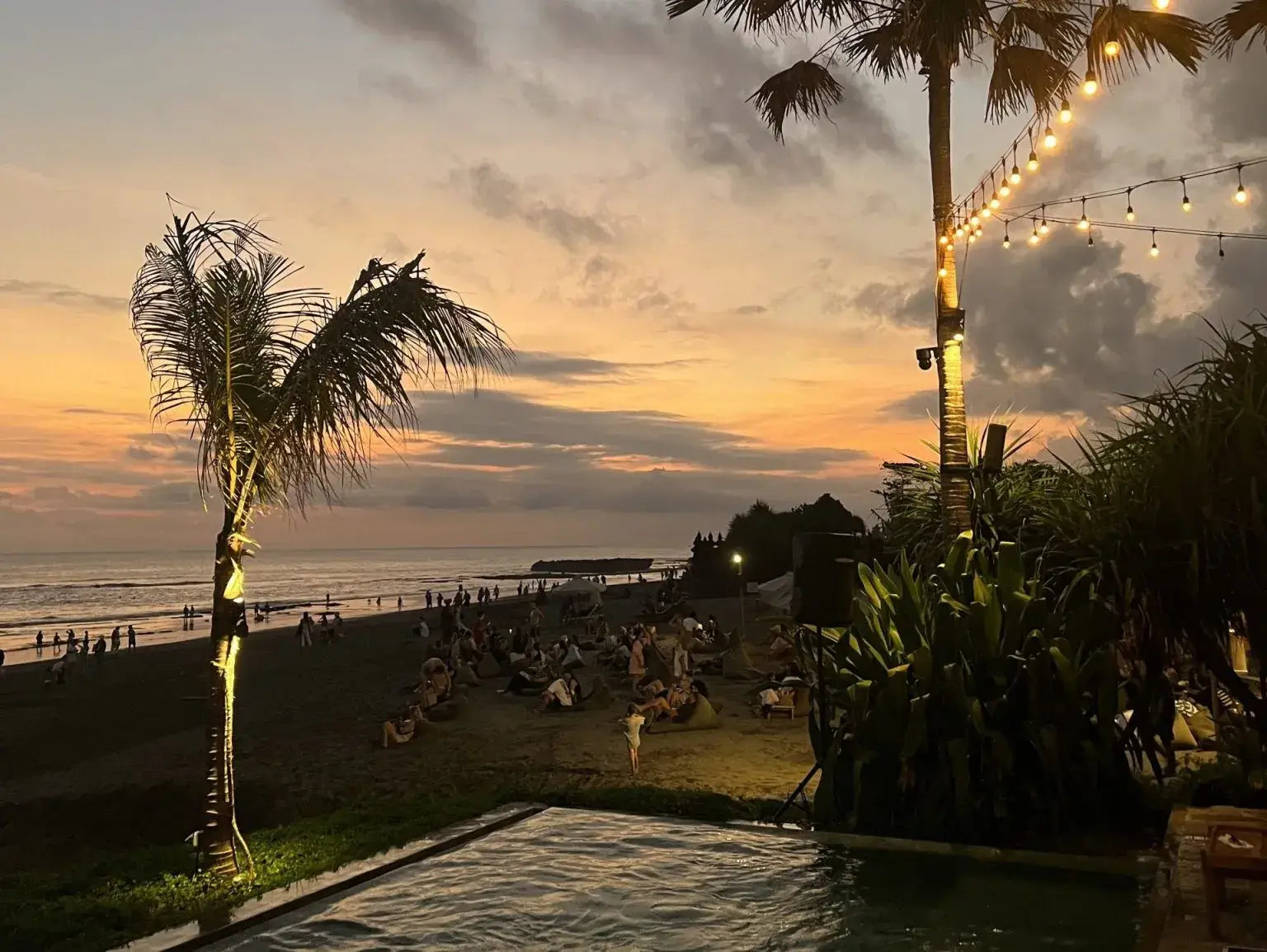 Bali - Stunning Canggu tropical beach at sunset with glowing string lights and palm trees.